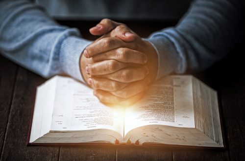 Folded hands over an open Bible