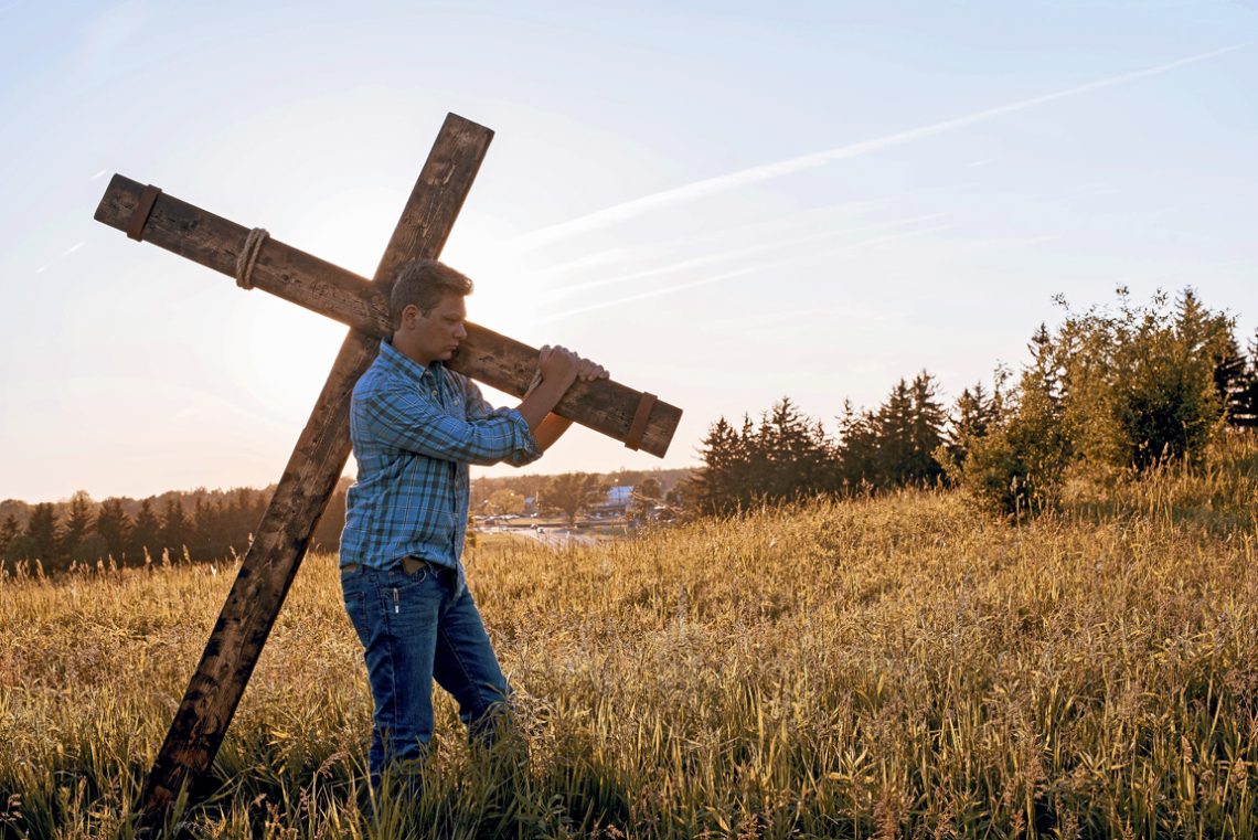 Male carrying a cross through the field