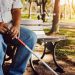Elderly blind man with a cane sits alone on a park bench