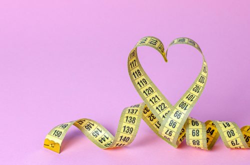 Yellow measuring tape in the shape of a heart on a pink background