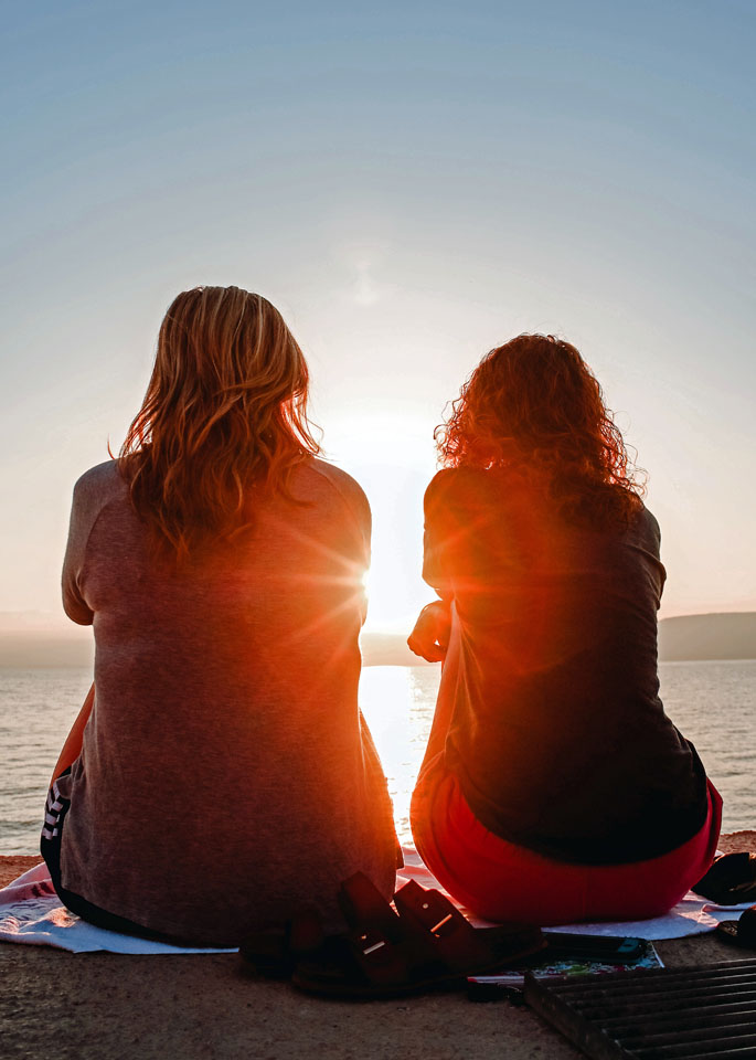 Two women sitting at the edge of a body of water