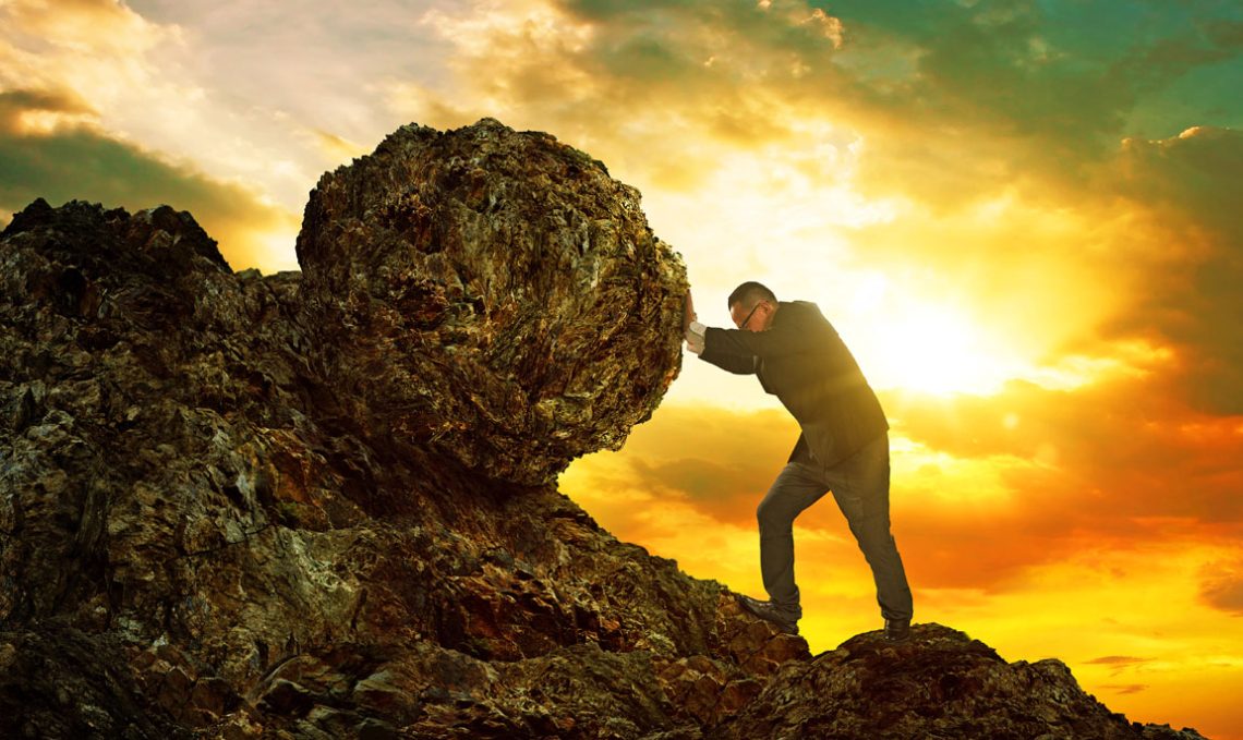 Business man pushing large stone uphill