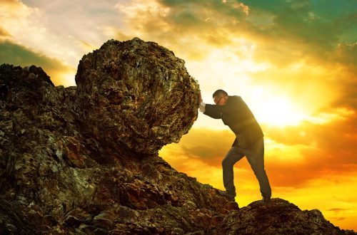 Business man pushing large stone uphill