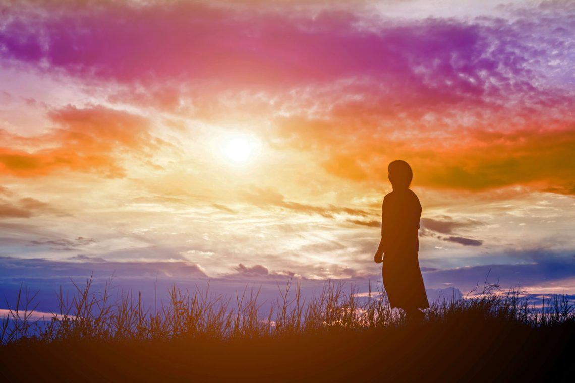 Silhouette of woman praying over beautiful sky background
