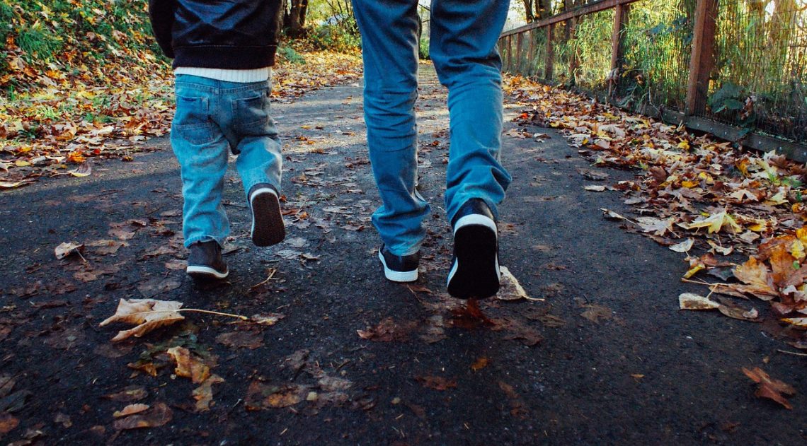 A dad and his son walking in the leaves on a path