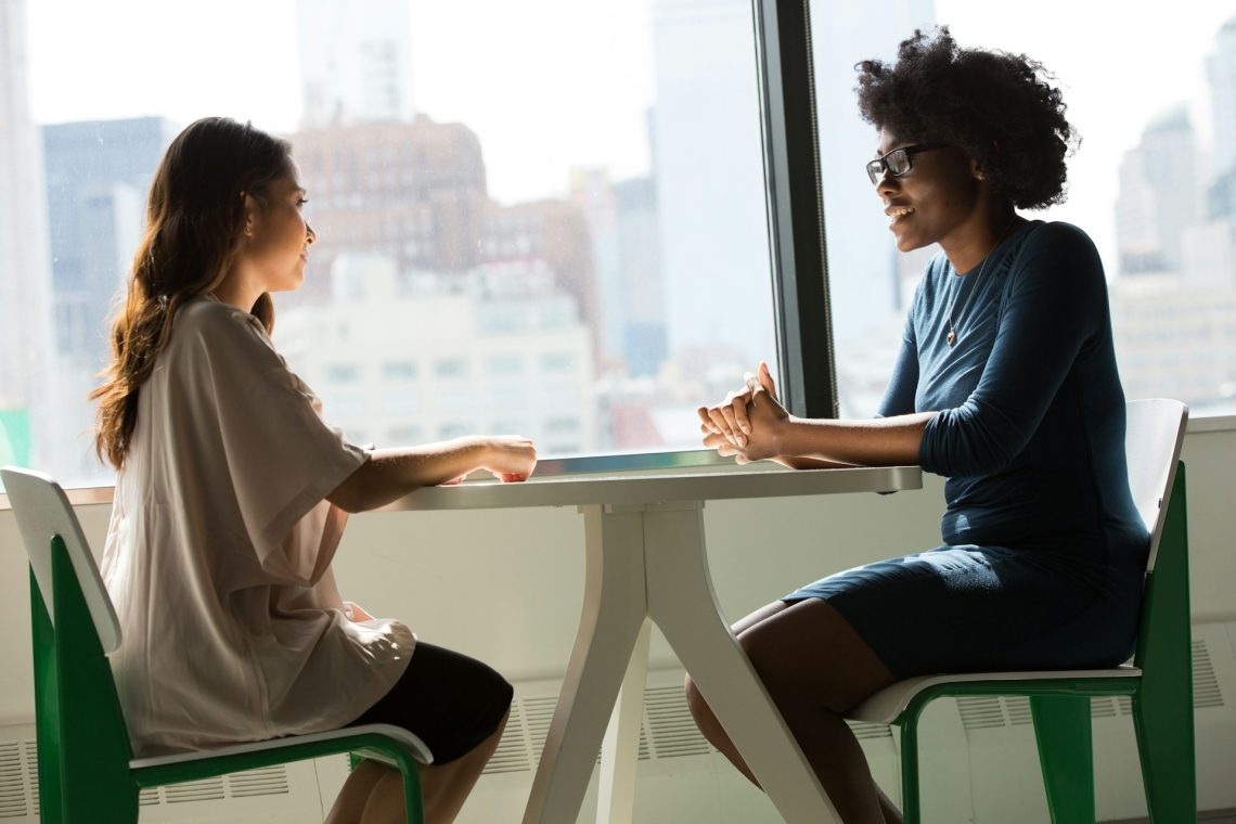 Two women talking in front of a window