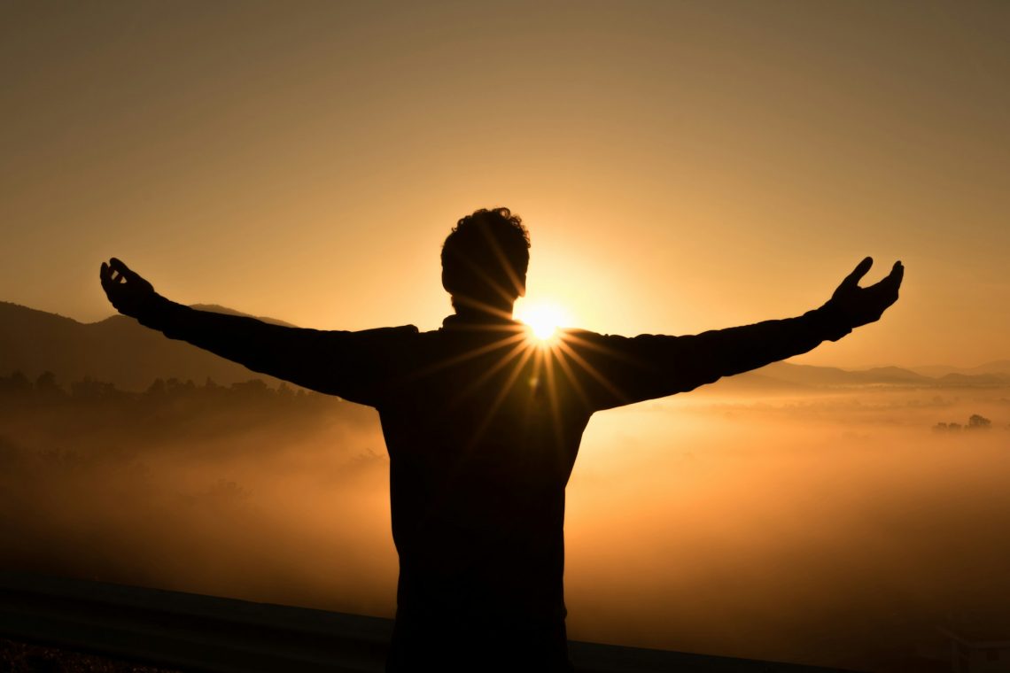 Man with arms outstretched in front of a sunrise