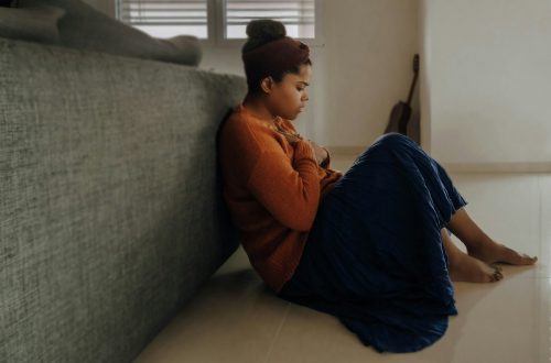 Young woman sitting on the floor in front of a couch, with her hands to her heart.