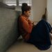 Young woman sitting on the floor in front of a couch, with her hands to her heart.