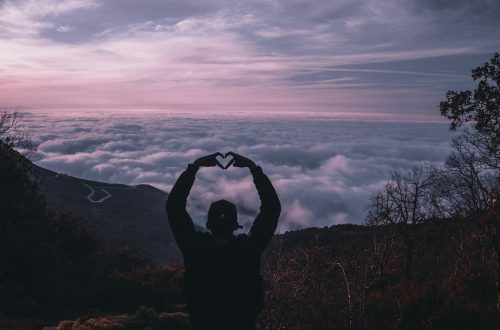 A man standing on a mountain creating a heart with his hands