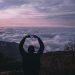 A man standing on a mountain creating a heart with his hands