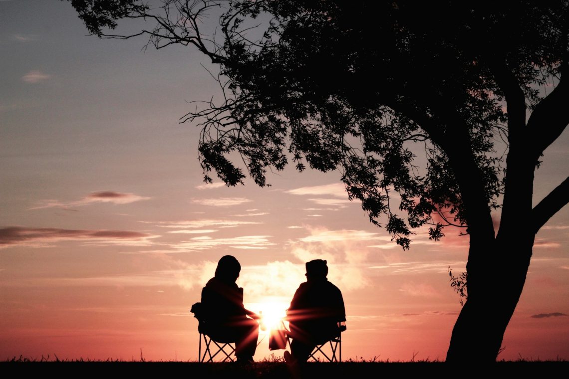 Two people sitting and talking in front of a sunset