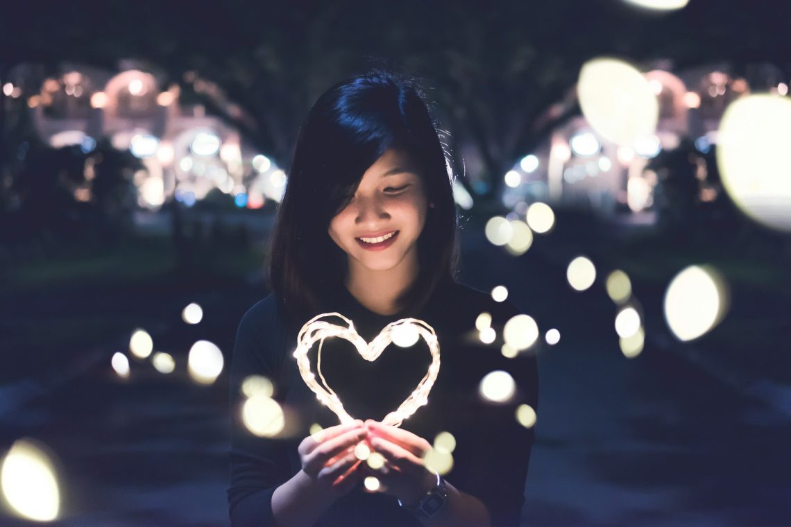 A young woman holding a heart made out of a light "rope"