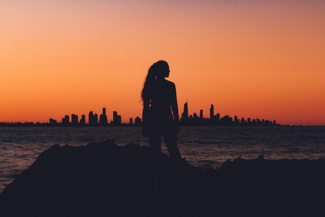 A silhouette of a woman standing in front of a sunset and skyline