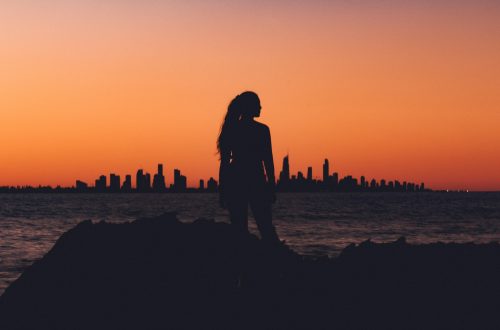A silhouette of a woman standing in front of a sunset and skyline