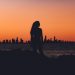 A silhouette of a woman standing in front of a sunset and skyline