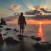 Man standing on a rock in the sea looking at the sunset
