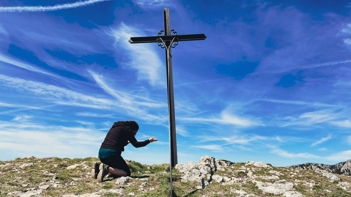 A woman kneeling before a cross on a ridge