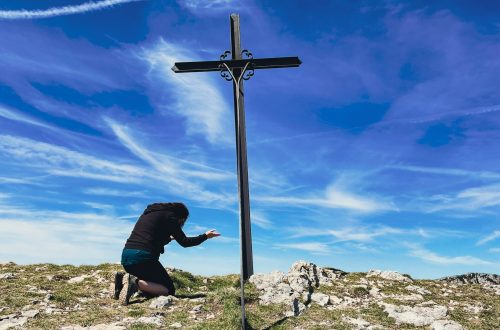 A woman kneeling before a cross on a ridge