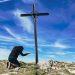 A woman kneeling before a cross on a ridge