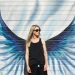 A woman standing in front of wings painted on a wall
