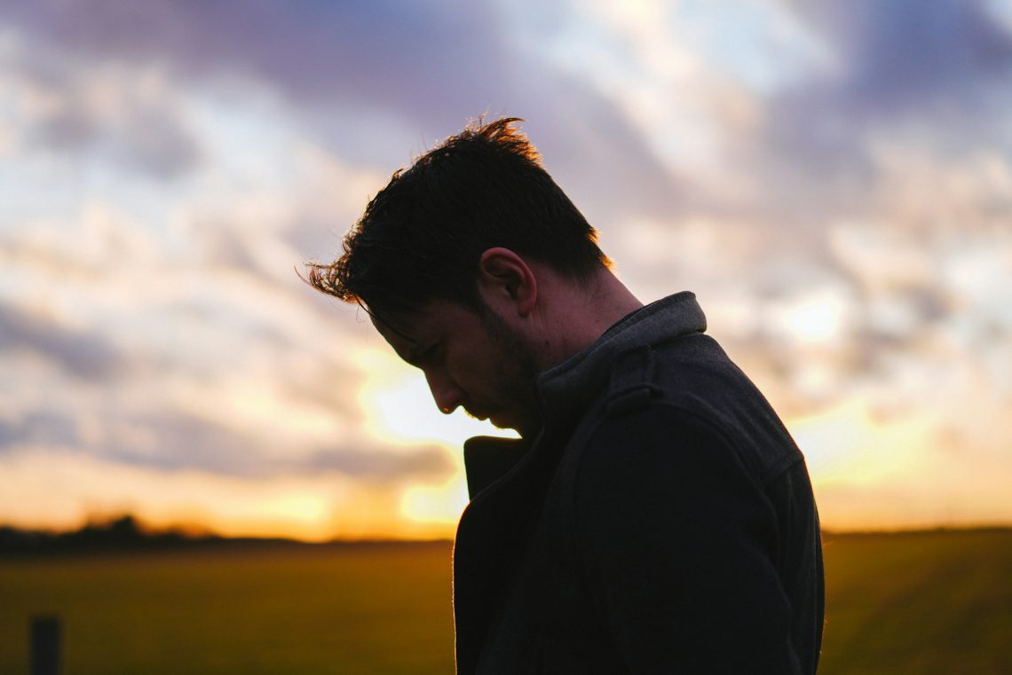 A man with head bowed in front of a sunset