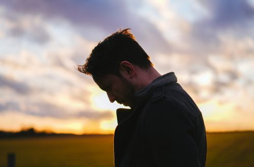 A man with head bowed in front of a sunset