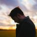 A man with head bowed in front of a sunset