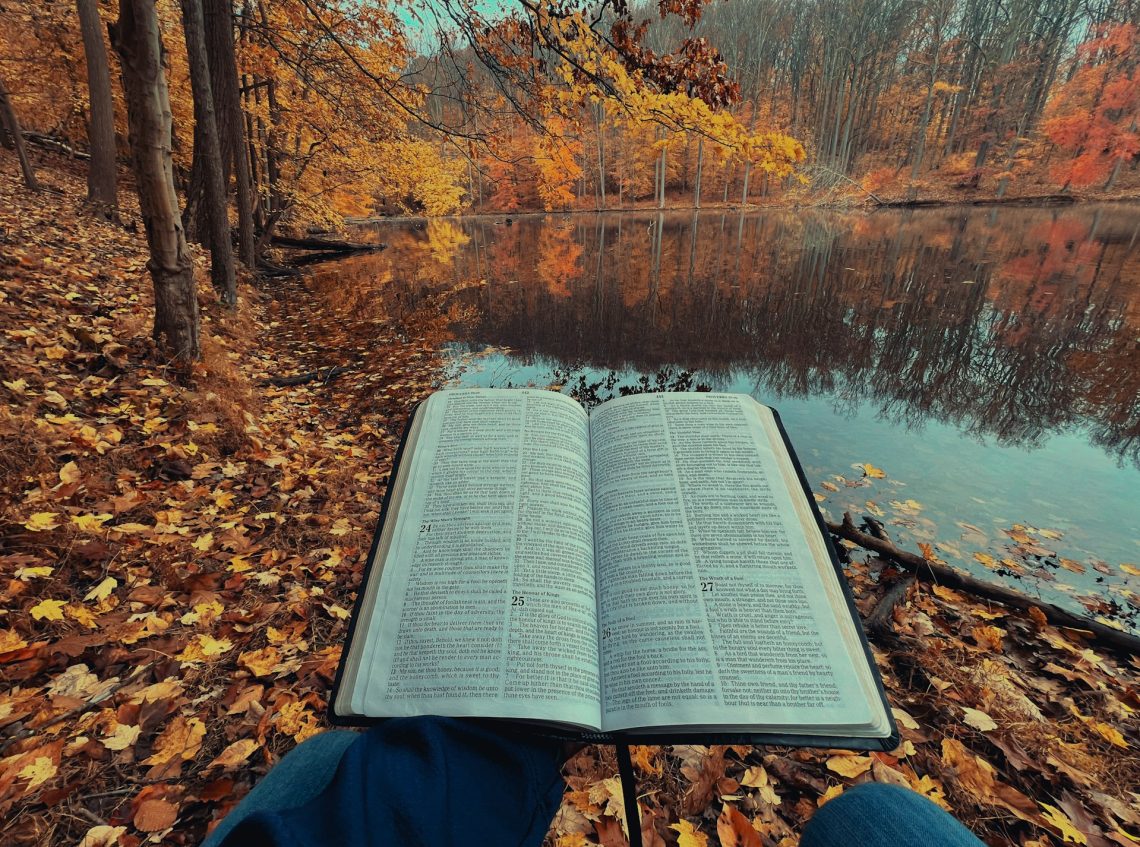 An open Bible in front of a lake and fall-colored forest