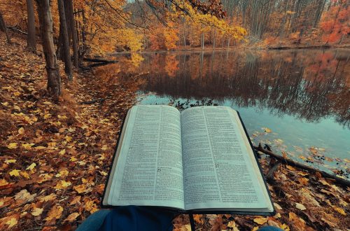 An open Bible in front of a lake and fall-colored forest