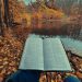 An open Bible in front of a lake and fall-colored forest
