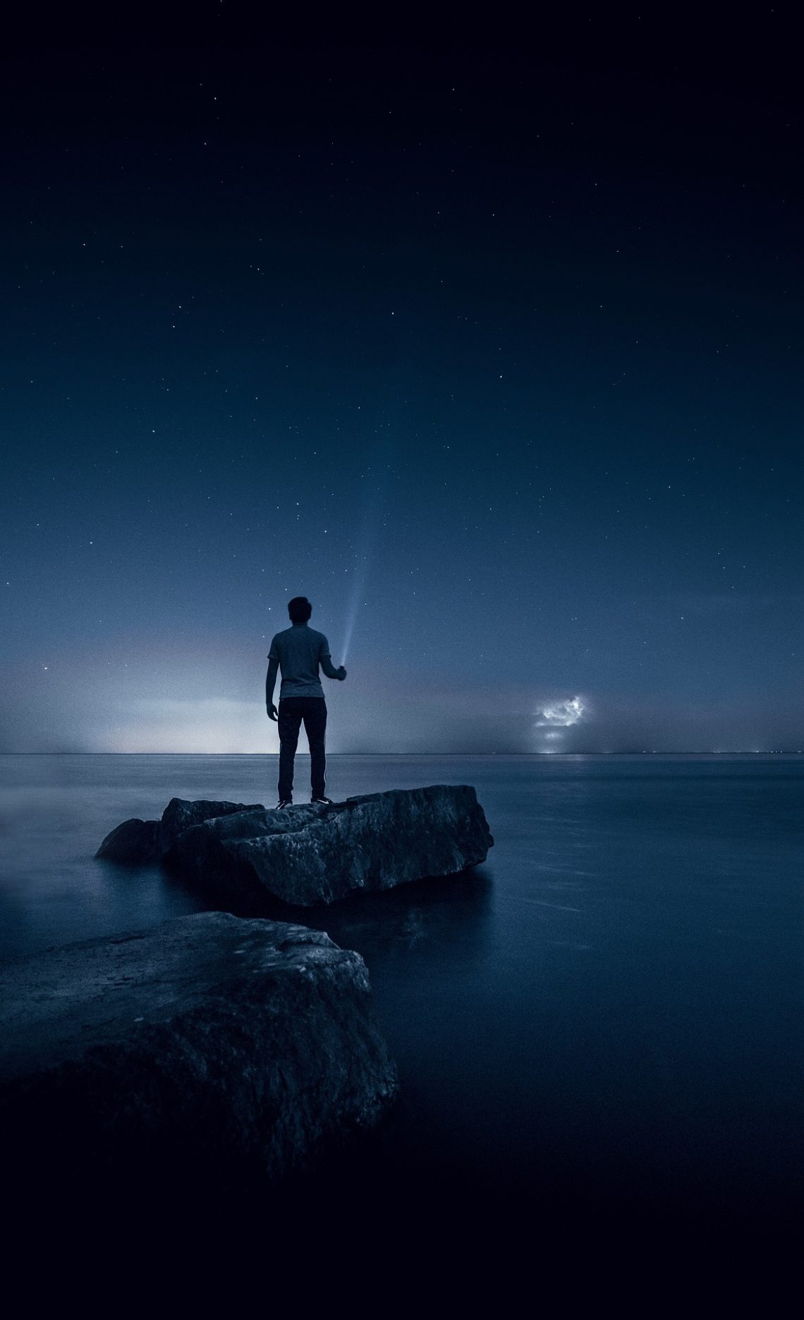 A man standing on rocks near the sea at night
