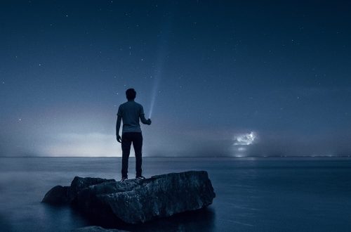 A man standing on rocks near the sea at night