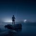 A man standing on rocks near the sea at night