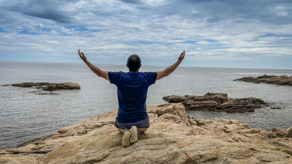 man kneeling on a rock by the sea
